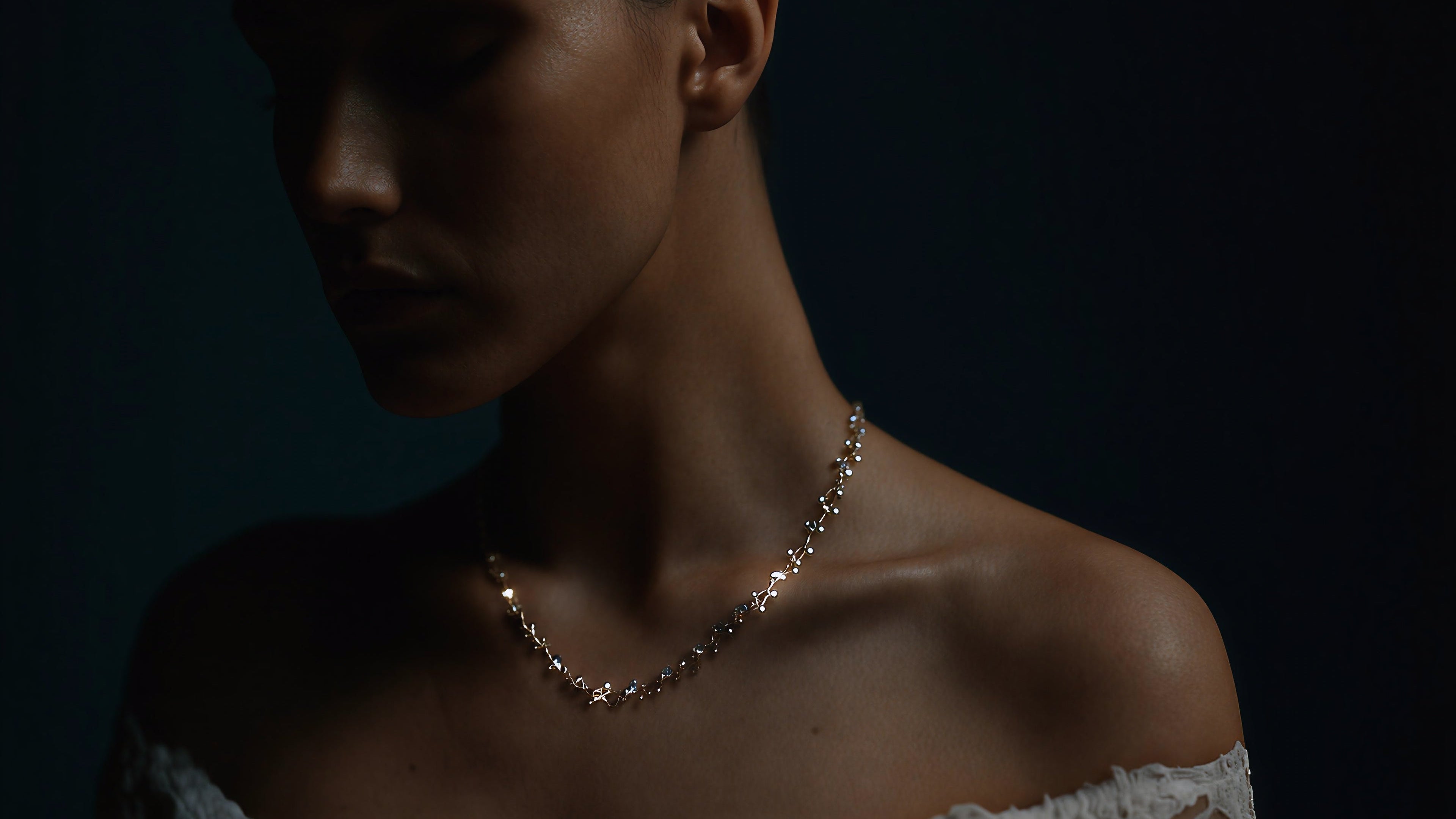 Woman wearing a delicate necklace against a dark background